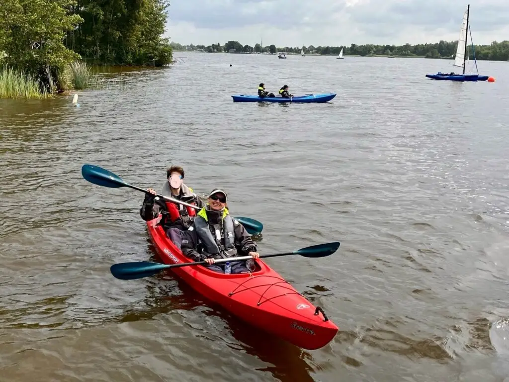 Marloes in een snelle rode kano met op de achtergrond een zeilboot en andere kano's.
